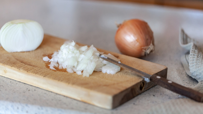 Onions on cutting board next to chopped onions and knife