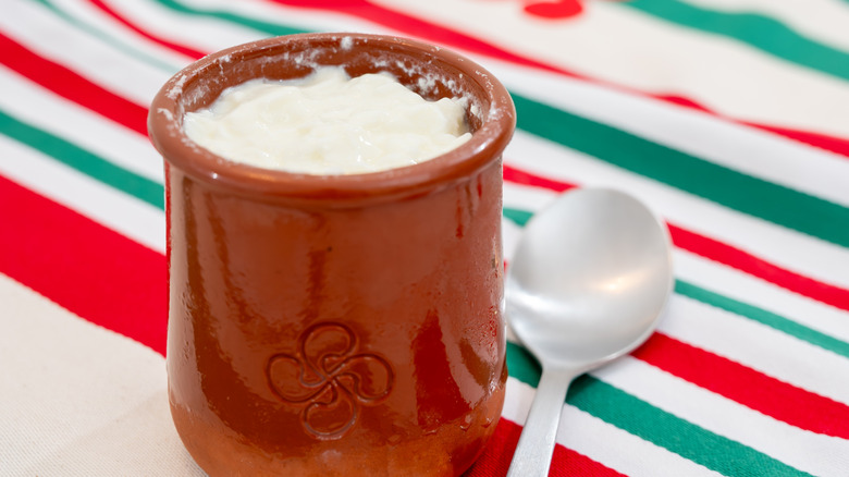 Curdled milk is visible in a mug with a spoon next to it on a striped background.