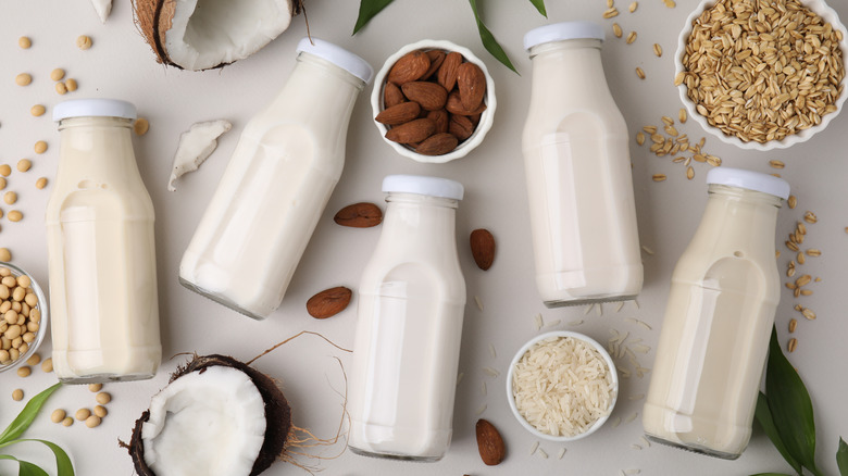 A variety of alternative milks are displayed in glass containers along with almonds, oats, soybeans, and coconuts.