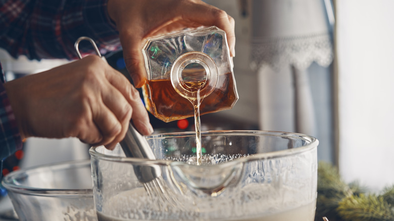 A person is pouring alcohol into an eggnog mixture.