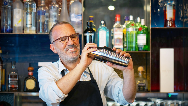 A man wearing an apron in a bar is shaking a cocktail.