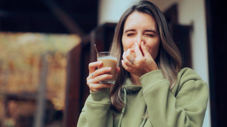 A woman is pinching her nose while holding a hot drink.