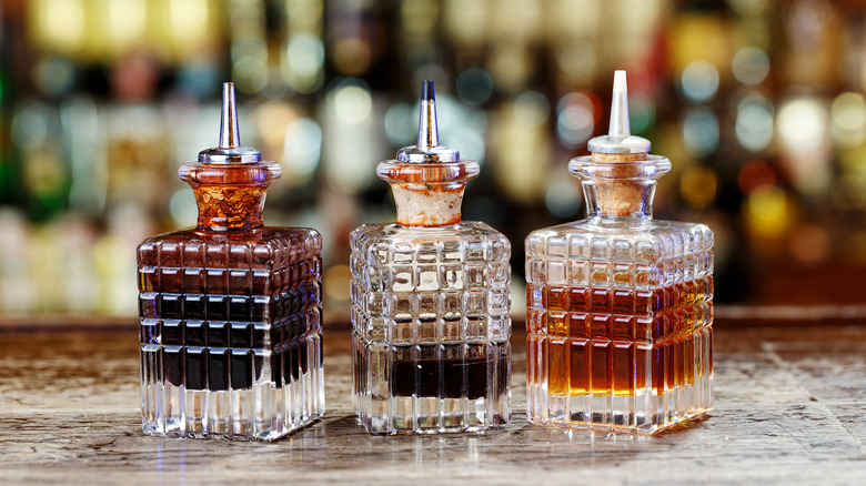 Three bottles containing cocktail bitters rest on a bar top.