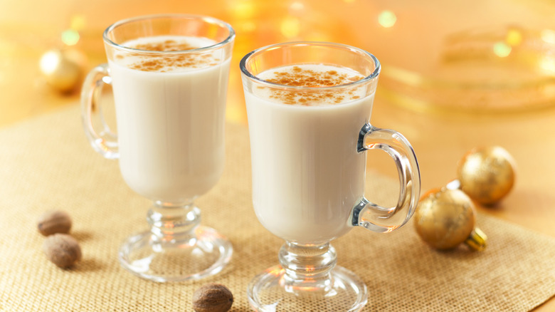 Two Irish coffee mugs are filled with eggnog on a festive golden background.