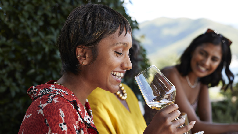 Person smiling as she takes a sip of wine in glass