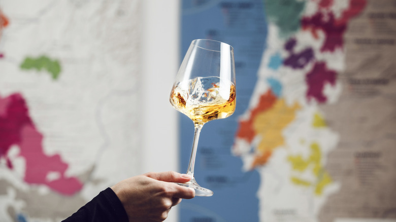 Hand swirling glass of white wine against wine maps