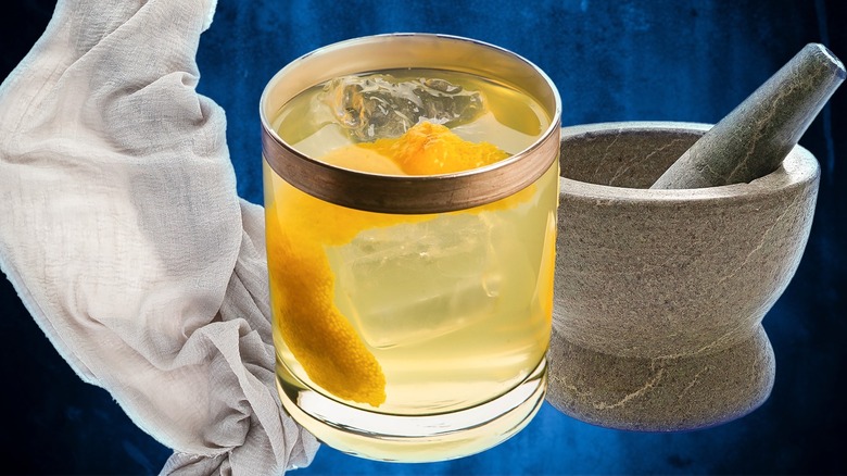 Infused orange vodka in a tasting glass next to a mortar pestle and cheesecloth against a blue background