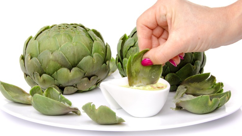 Hand dipping artichoke leaf in sauce