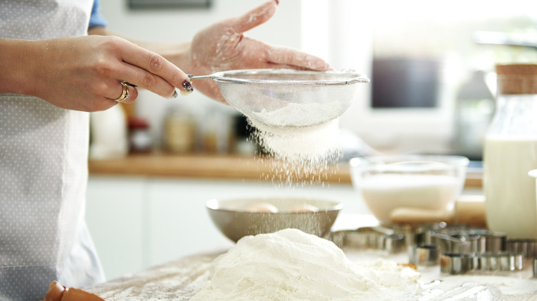 Woman sifting flour on kitchen counter