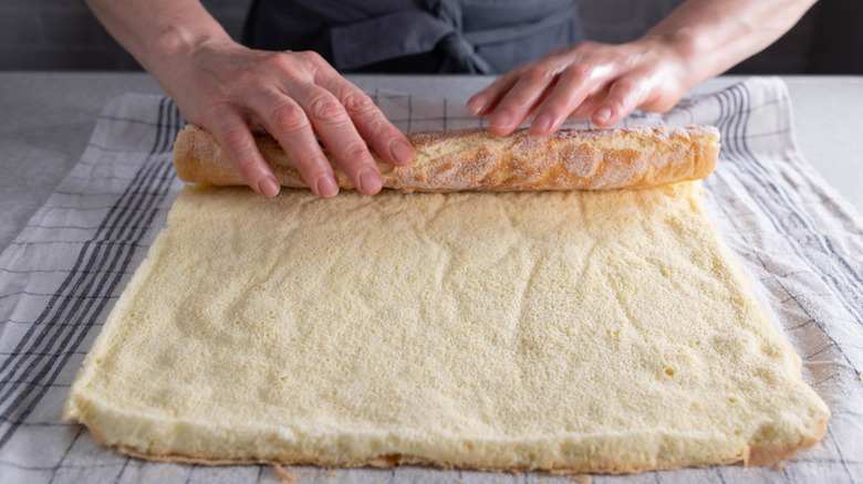 Hands rolling up sponge cake on a dish towel