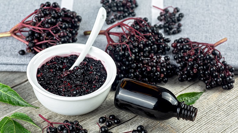 Fresh elderberries on a table next to a bowl of mashed berries