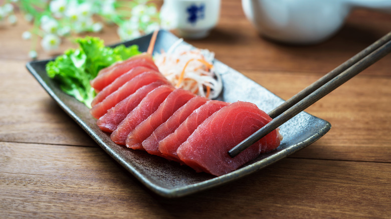 Plate of tuna sashimi with chopsticks holding one piece