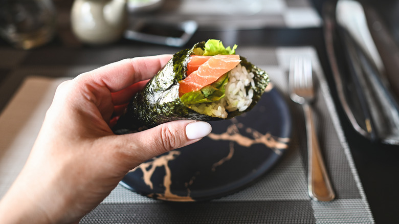 Hand holding temaki sushi roll with salmon