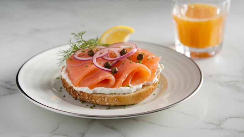 Half of seeded lox bagel on white plate on marble counter