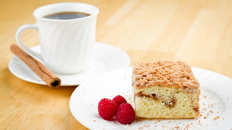 Coffee cake and raspberries on white plate in front of white coffee mug