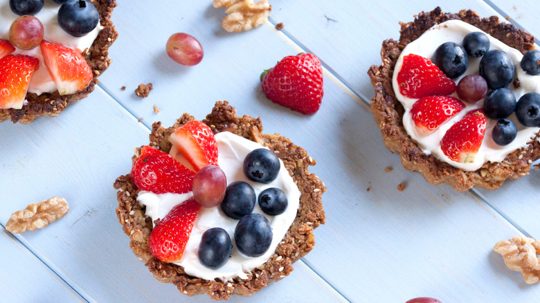 Fruit and granola breakfast tartlets with strawberries, blueberries, grapes on white counter