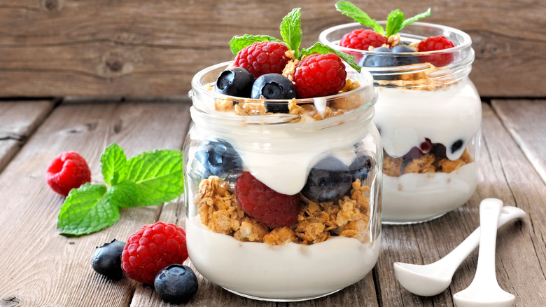 Two fruit and yogurt parfaits in glass jars on wooden table