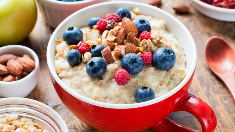 Red mug of oatmeal with berries and nuts on wooden counter