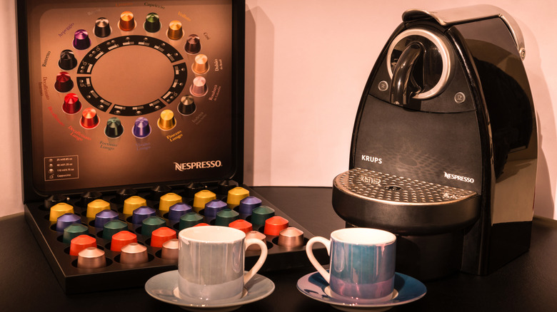 Two empty cups and saucers on a table with Nespresso machine and box of Nespresso pods