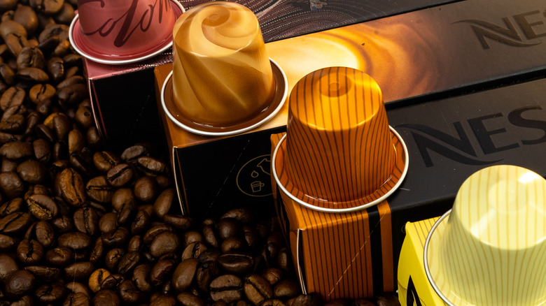 Four Nespresso pods atop Nespresso sleeves sitting atop coffee beans