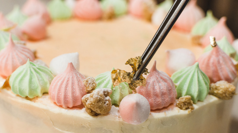 closeup of tweezer applying gold leaf flakes to meringue