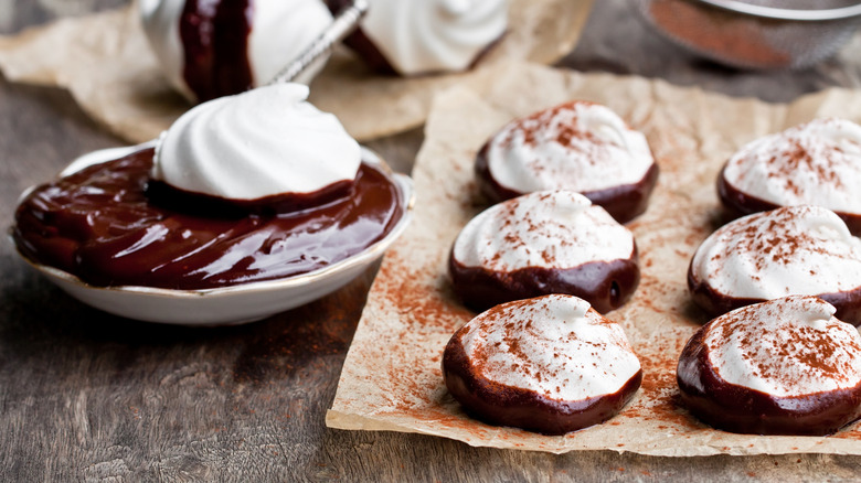 white meringues dipped in dark chocolate sitting on sheet of parchment paper