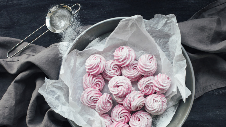 pink meringues in a bowl covered in powdered sugar