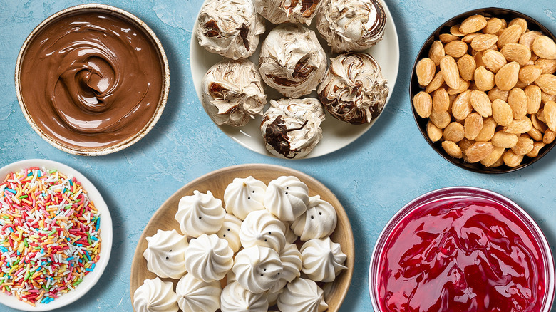 plates of meringue cookies surrounded by toppings, chocolate, and jam