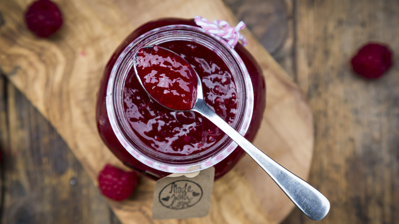 overhead shot of spoonful of jam resting on glass jar with raspberries in the background