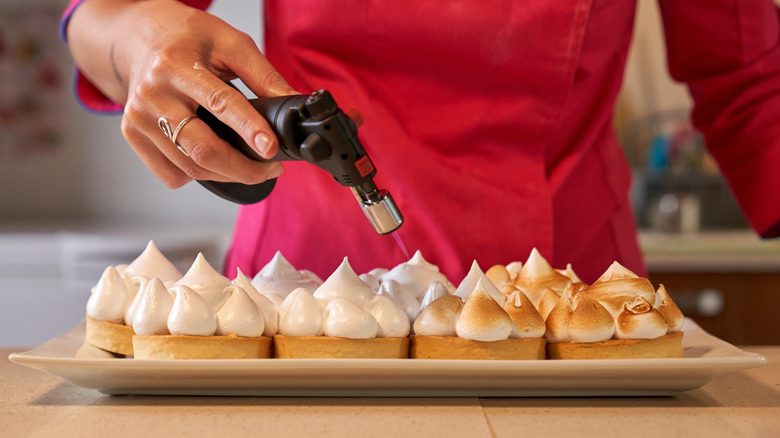 person hand torching meringue on top of tartlets