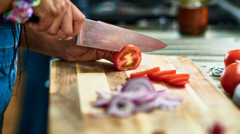 Person slicing tomatoes and red onion with knife