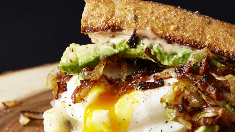 breakfast sandwich with egg, bacon, onions, and avocado