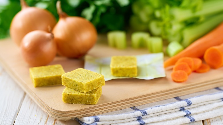 Bouillon cubes on wooden cutting board with vegetables in background