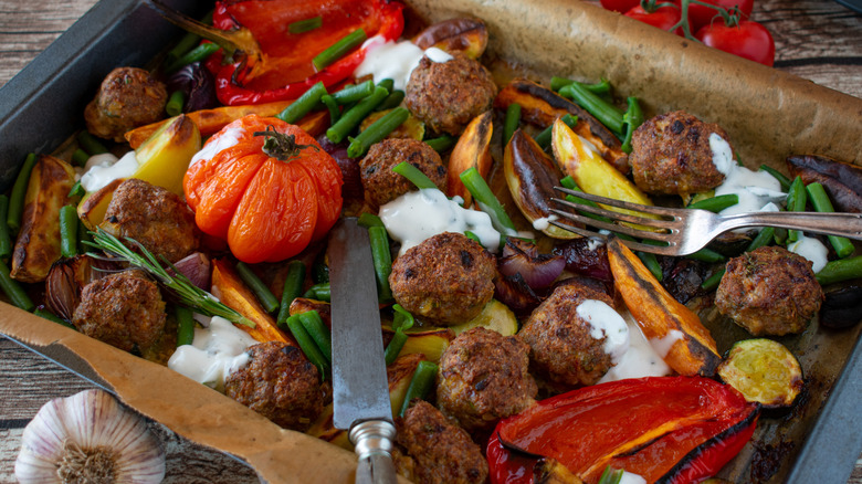 Meatballs and variety of vegetables on black sheet pan with fork and knife