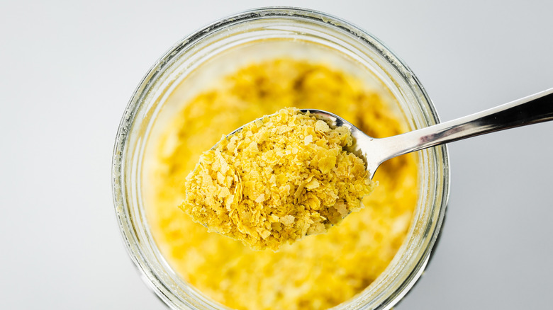 spoonful of nutritional yeast hovering above a glass bowl full of it