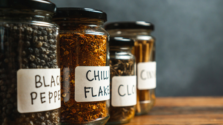 Jars of spices labeled back pepper, chili flakes, cloves, and cinnamon