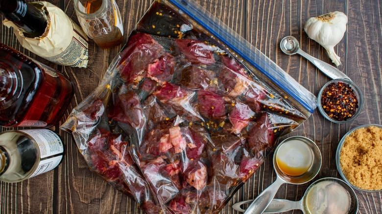 Whiskey-based marinade steak in a plastic bag with spices and bottles