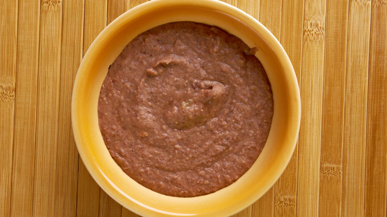 Refried beans in yellow bowl on wooden table