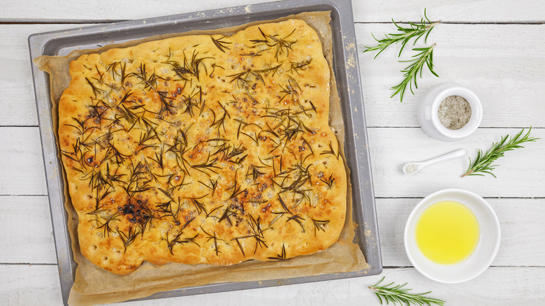 Herby focaccia on pan covered in rosemary needles