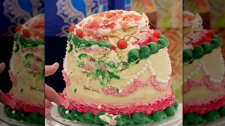 A collapsed multitiered cake with smeared green, white, and pink frosting, collapsed cherries on one side
