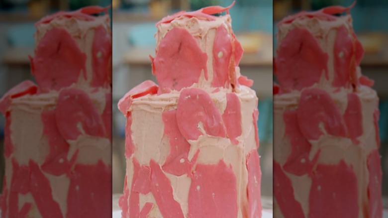 A two tiered cake adorned messily with a peach-colored frosting and what appears to be almost fish-shaped pieces of decorative fondant added on top