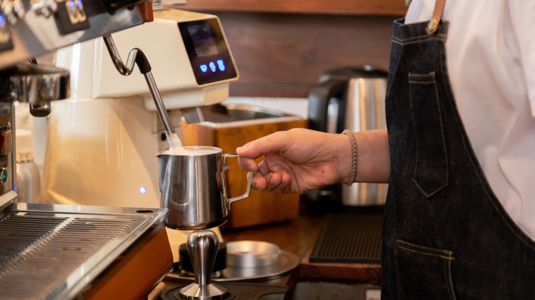 Barista frothing milk with stainless steel milk pitcher