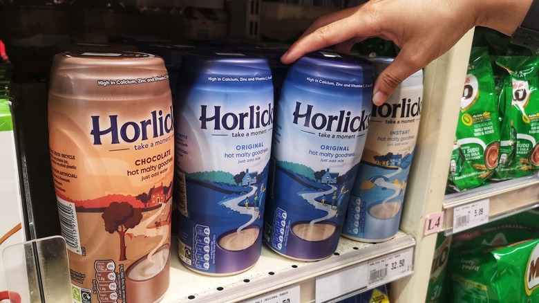 Hand removing container of Horlicks from grocery store shelf