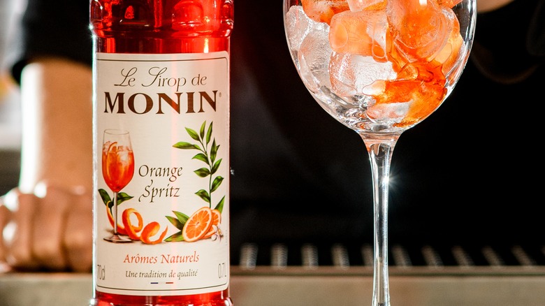 Bottle of Monin orange syrup next to orange cocktail