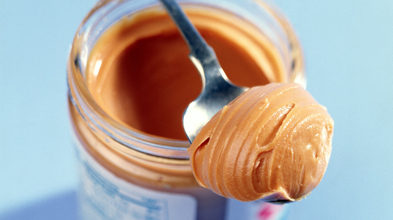 Spoonful of creamy peanut butter resting on top of open jar