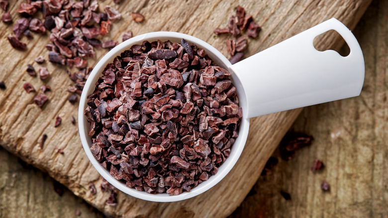 cacao nibs in measuring cup on wooden surface