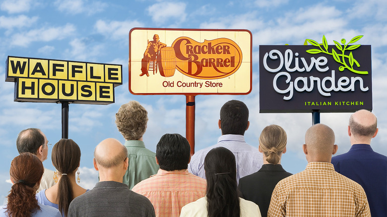 Group of people facing various chain restaurant signages against the sky