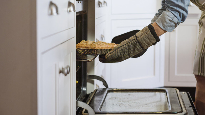 Gloved hands taking pie out of the oven.