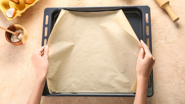 Two hands placing parchment paper in a pan.