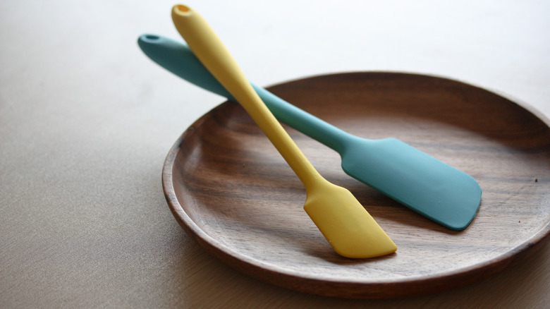 Yellow and blue rubber spatulas on wooden plate.